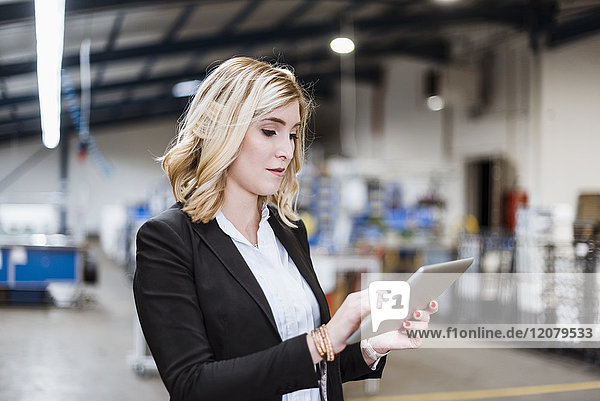 Blonde Geschäftsfrau steht in der Werkstatt  mit digitalem Tablett
