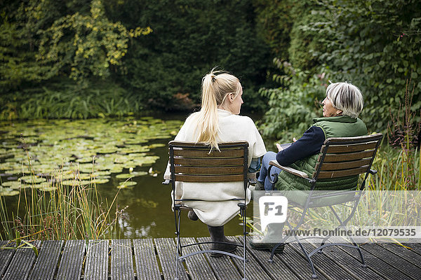 Young woman with her grandmother sitting on jetty at garden pond