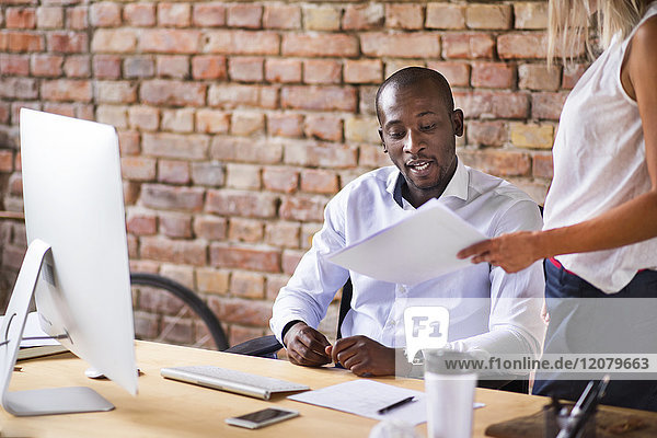 Colleague showing paper to man at desk in office