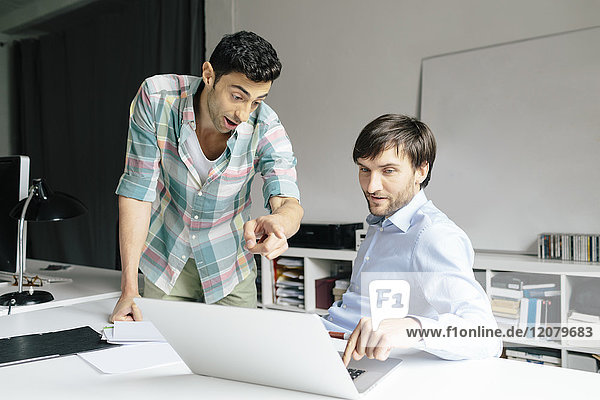 Zwei Geschäftsleute mit Laptop am Schreibtisch im Büro bei der Diskussion