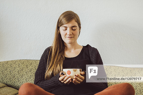 Woman with eyes closed sitting on couch with tea cup