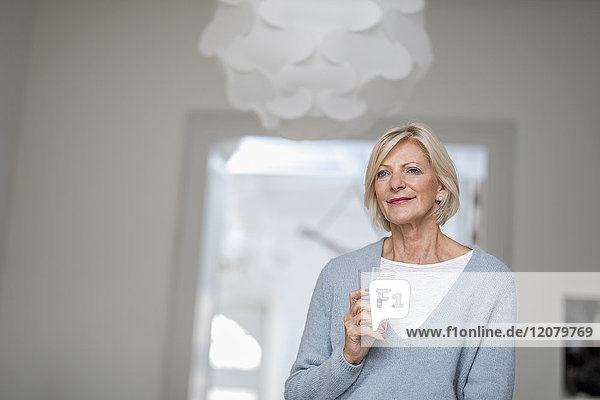 Porträt einer entspannten Seniorin mit einem Glas Wasser zu Hause