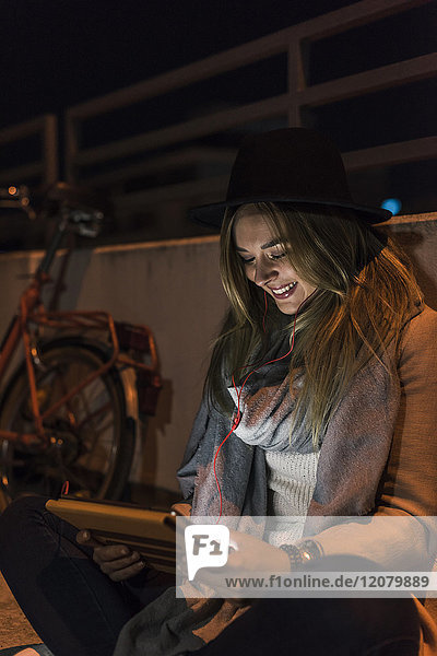 Lächelnde junge Frau in der Stadt mit Tablette bei Nacht
