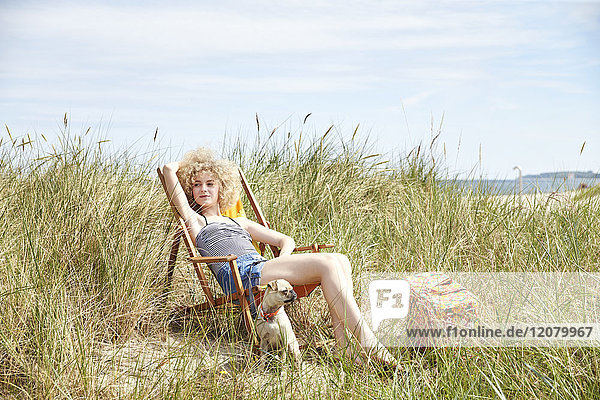 Porträt einer jungen Frau  die auf einem Strandkorb in den Dünen sitzt und etwas beobachtet.
