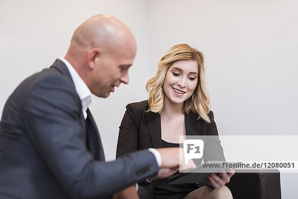 Businessman and businesswoman sitting on couch sharing tablet