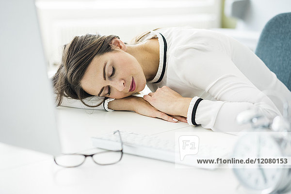 Überarbeitete Frau schläft auf dem Schreibtisch im Büro