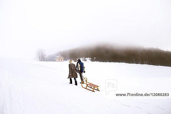 Rückansicht des Seniorenpaares mit Schlittenwanderung nebeneinander in verschneiter Landschaft