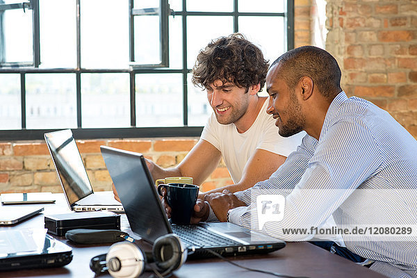 Two young businessmen working together in co-working space  using laptops