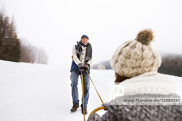 Glückliches Seniorenpaar beim Schlittenfahren in verschneiter Landschaft