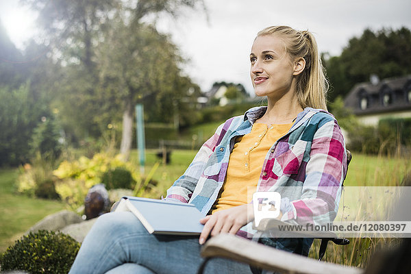 Smiling young woman with book relaxing in garden