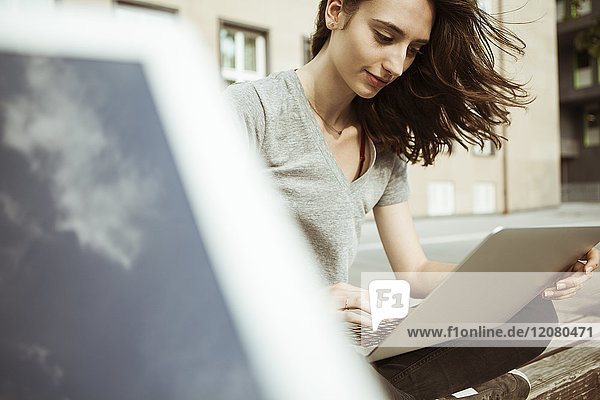 Young woman sitting on bench using laptop