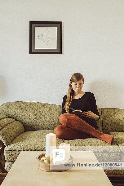 Woman sitting on couch in the living room writing in notebook