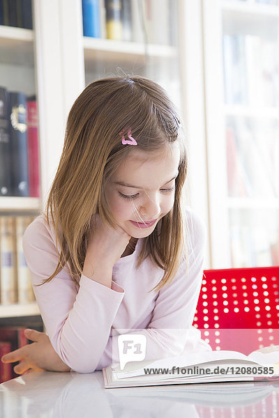 Portrait of smiling little girl at table reading a book