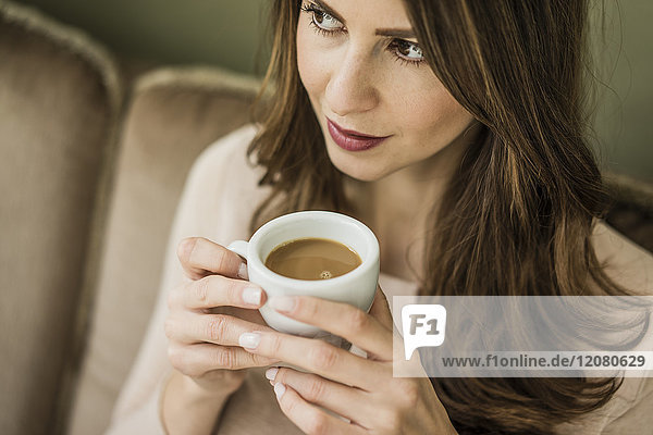 Porträt einer Frau  die auf der Couch sitzt und eine Tasse weißen Kaffee trinkt.