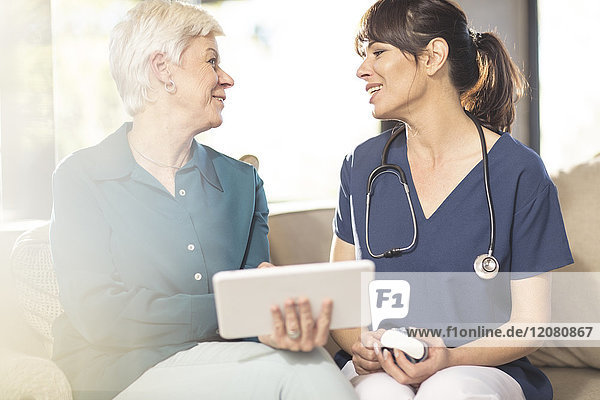 Krankenschwester im Gespräch mit Seniorin mit Tablette zu Hause