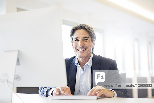 Porträt eines glücklichen Geschäftsmannes am Schreibtisch im Büro