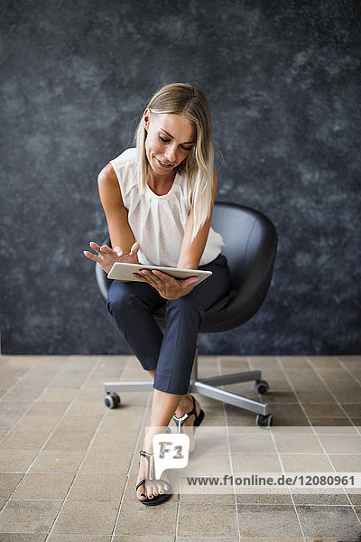 Businesswoman sitting in armchair using tablet