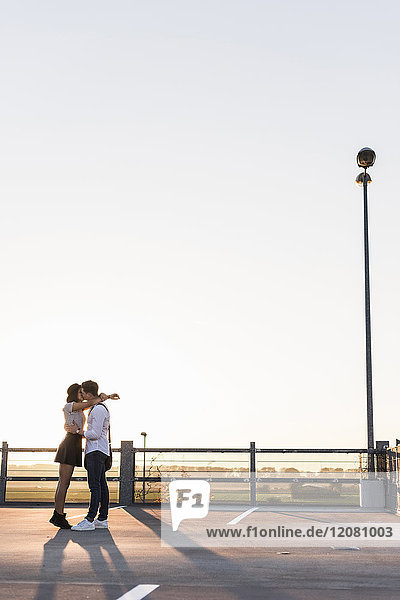Junges Paar  das sich bei Sonnenuntergang auf der Parkebene küsst.
