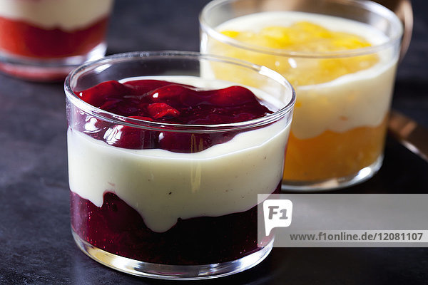 Rote und gelbe Früchtekompott mit Vanillesauce in Gläsern geschichtet