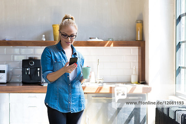 Geschäftsfrau steht mit Kaffeetasse in der Küche und schaut auf das Tablett.