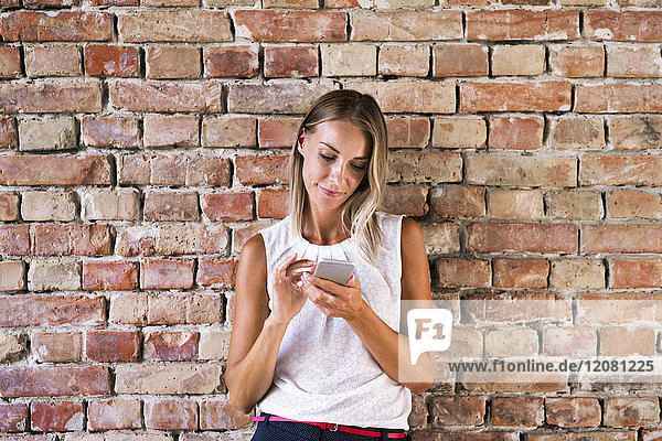 Businesswoman using cell phone at brick wall