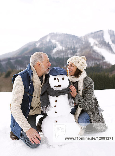 Seniorenpaar mit Schneemann in Winterlandschaft