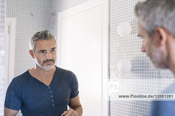 Erwachsener Mann  der in den Badezimmerspiegel schaut