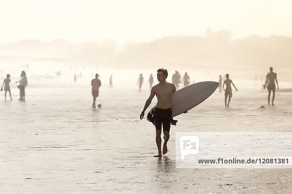 Indonesien  Bali  Surfer mit Surfbrett am Strand bei Sonnenuntergang