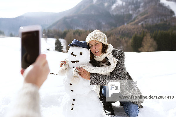 Senior man taking picture of his wife with snowman