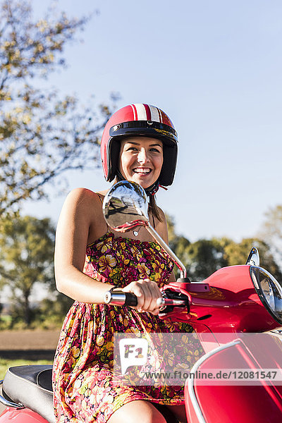 Porträt der glücklichen jungen Frau auf dem Motorroller