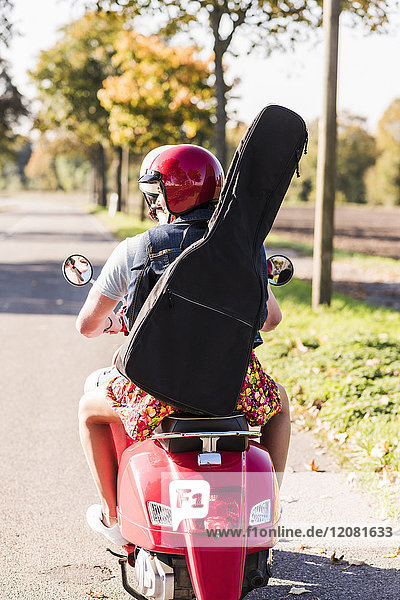 Junges Paar auf einem Motorroller mit Gitarrentasche auf dem Rücken