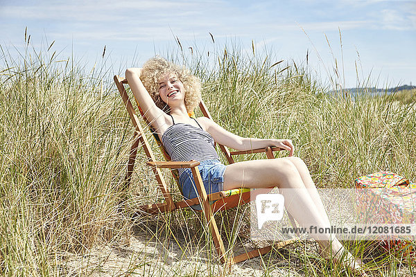 Portrait of happy young woman sitting on beach chair in the dunes