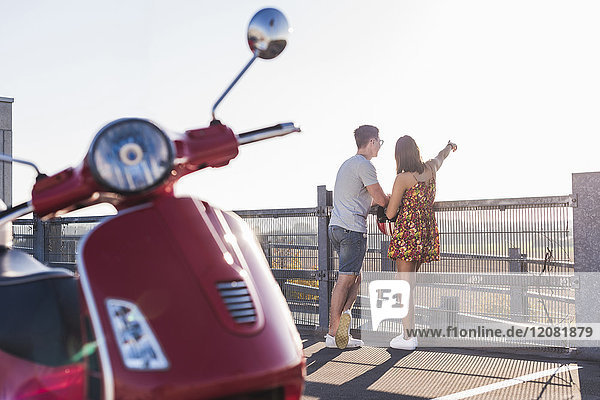 Junges Paar auf Parkebene stehend mit Motorroller im Vordergrund