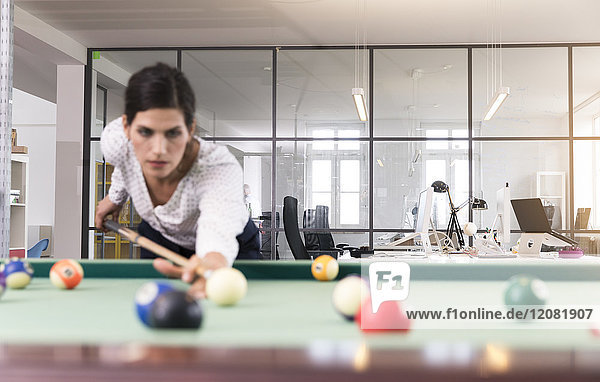 Entschlossene Geschäftsfrau beim Billard spielen im modernen Büro
