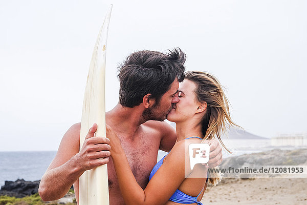 Junges Paar mit Surfbrettkuss am Strand