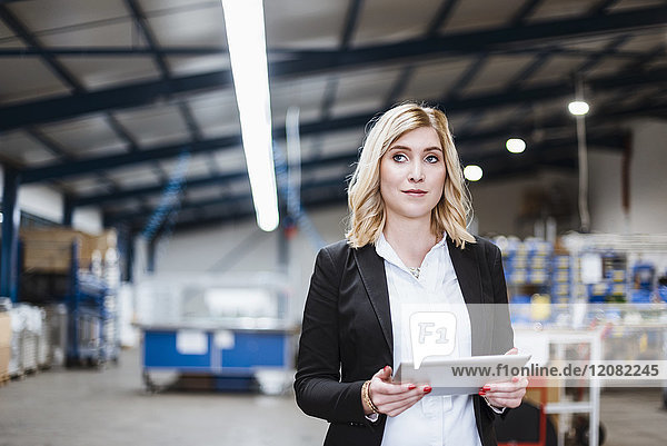 Blond businesswoman standing in shop floor  using digital tablet