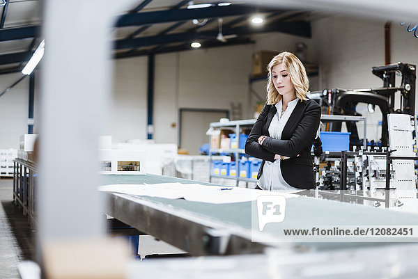 Blond businesswoman standing on shop floor  looking at plans