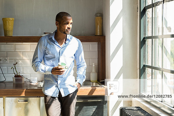 Young entrepreneur standing in company kitchen  drinking coffee