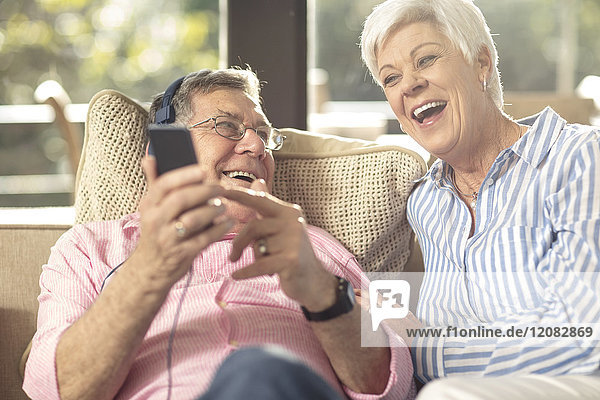 Happy senior couple with cell phone and headphones on couch at home