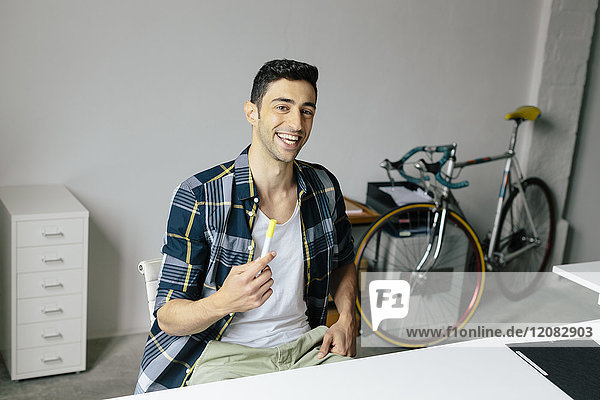 Porträt eines glücklichen jungen Mannes am Schreibtisch im Büro