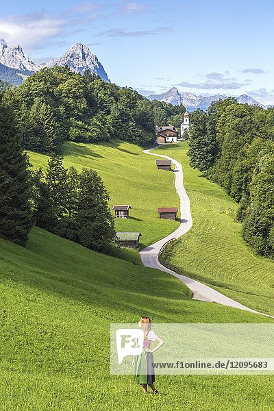 A girl in Typical Bayern dress walking in front of Wamberg village  with Mount Zugspitze and Waxenstein on the background. Garmisch Partenkirchen  Bayern  Germany.