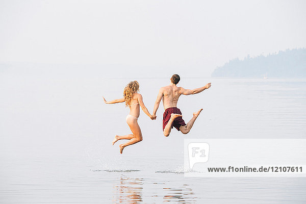 Junges Paar am Strand  Händchenhalten  Springen  mittlere Luft  Rückansicht