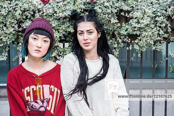 Portrait of two young stylish women sitting on city bench
