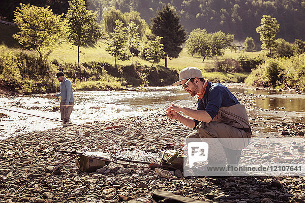 Young fisherman crouching with fishing rod by river Mozirje Brezovica Slovenia
