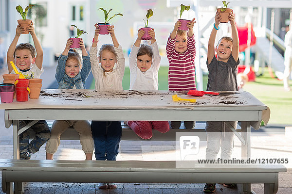 Mädchen und Jungen in der Vorschule  Porträt  das Topfpflanzen am Picknicktisch hochhält