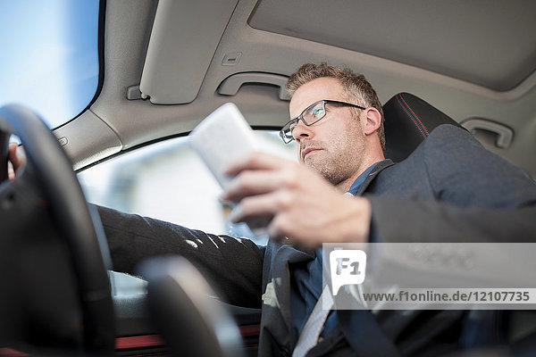 Businessman driving car  holding smartphone  low angle view