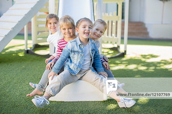 Mädchen und Jungen in der Vorschule  Porträt sitzend auf einer Spielplatzrutsche im Garten