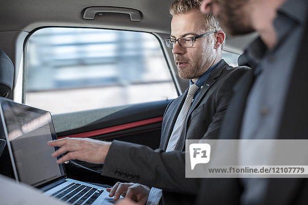Two businessmen sitting in back of car  looking at laptop screen