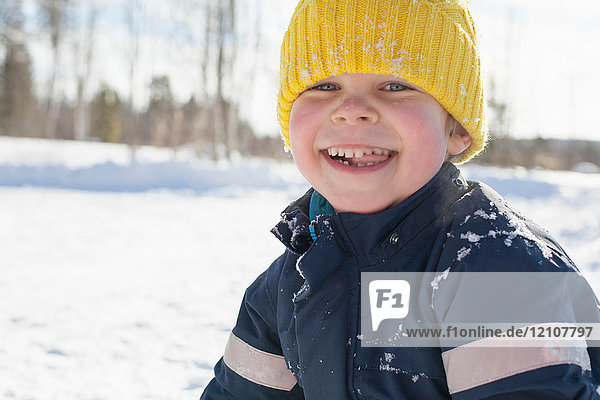 Porträt eines glücklichen Jungen mit gelber Strickmütze in schneebedeckter Landschaft