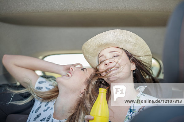 Zwei junge Frauen sitzen lachend auf dem Rücksitz eines Autos